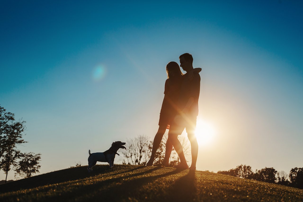 Young people family hugging standing on hilltop looking at the little dog